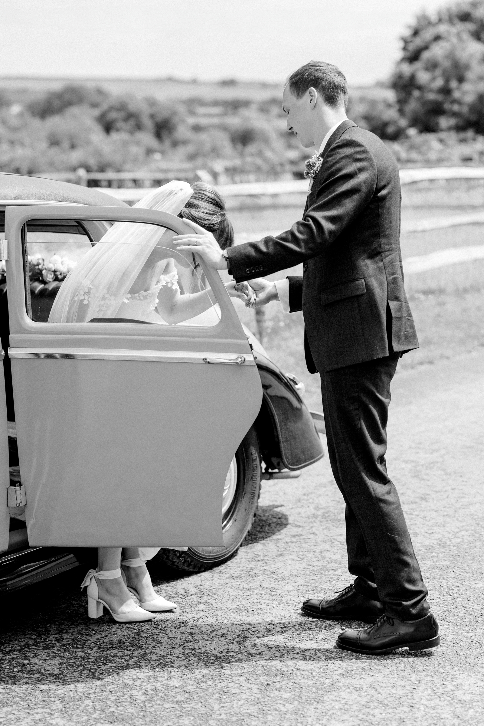 Groom helps bride out of vintage wedding car at South Stoke Barn Wedding Venue