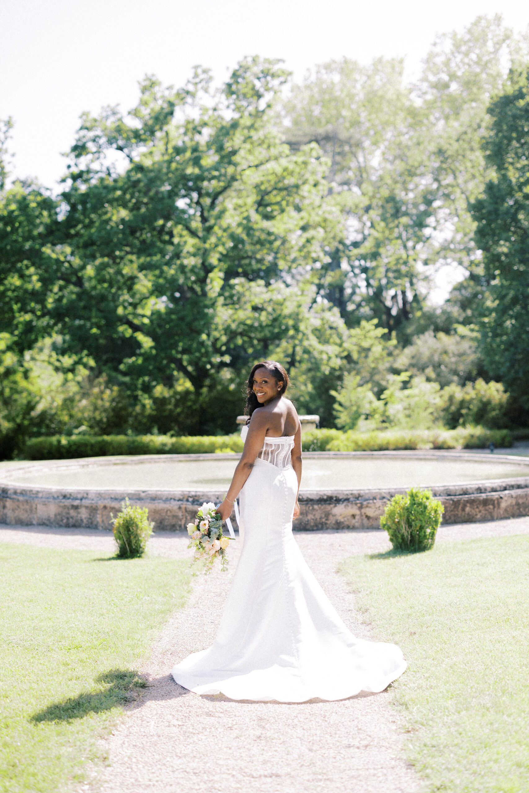 Bride stands by the fountain at Chateau de Valmousse on her wedding day